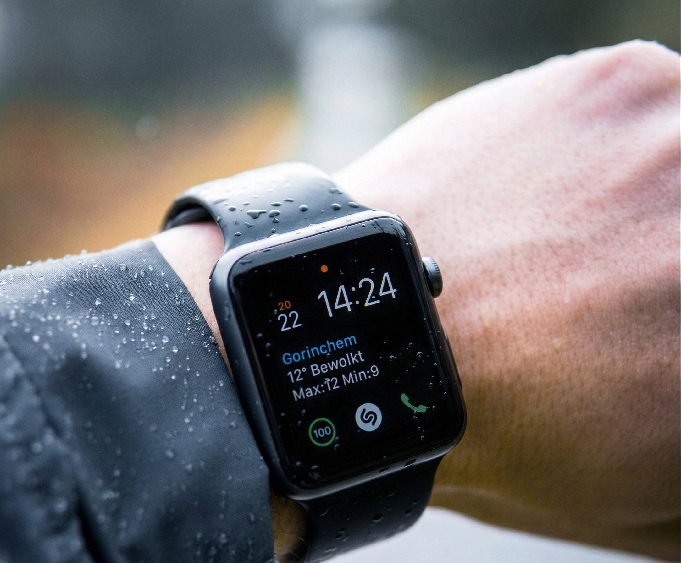 Person wearing a black smartwatch showing time and weather, with rain droplets on the screen and wristband