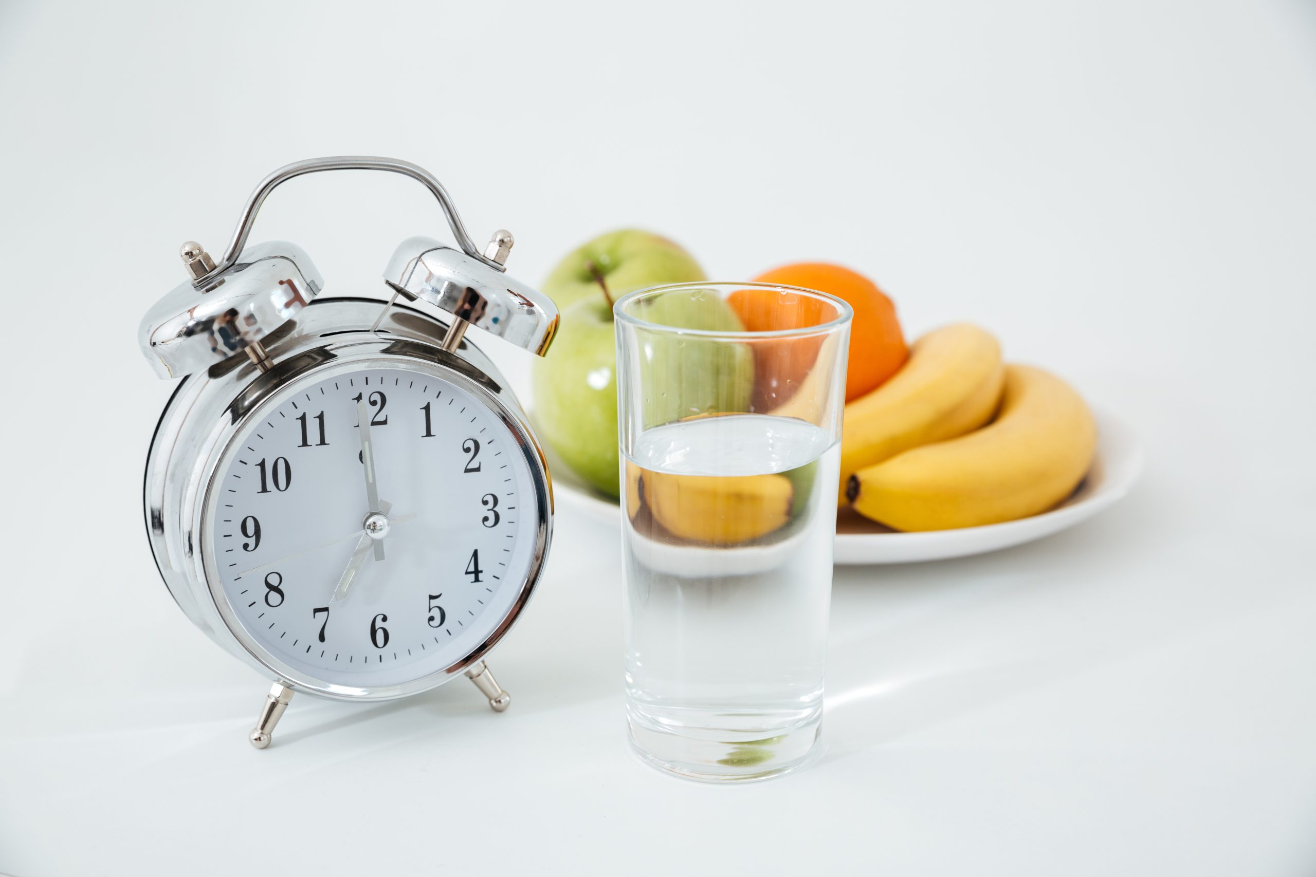 Alarm clock beside glass of water and plate of fruit, symbolising healthy morning routine.